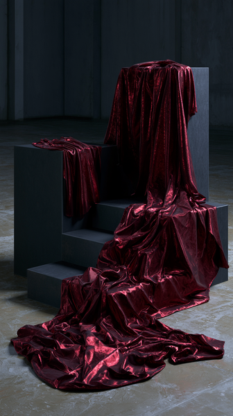 A high-fashion magazine editorial featuring deep crimson red luxury silk fabric draping elegantly over a minimalist matte-black concrete pedestal,…