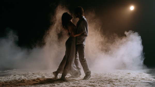 A poetic and emotional 16:9 contemporary dance film trailer scene. A fluid, sculptural duet dance performance on a minimalist dark stage covered in a…