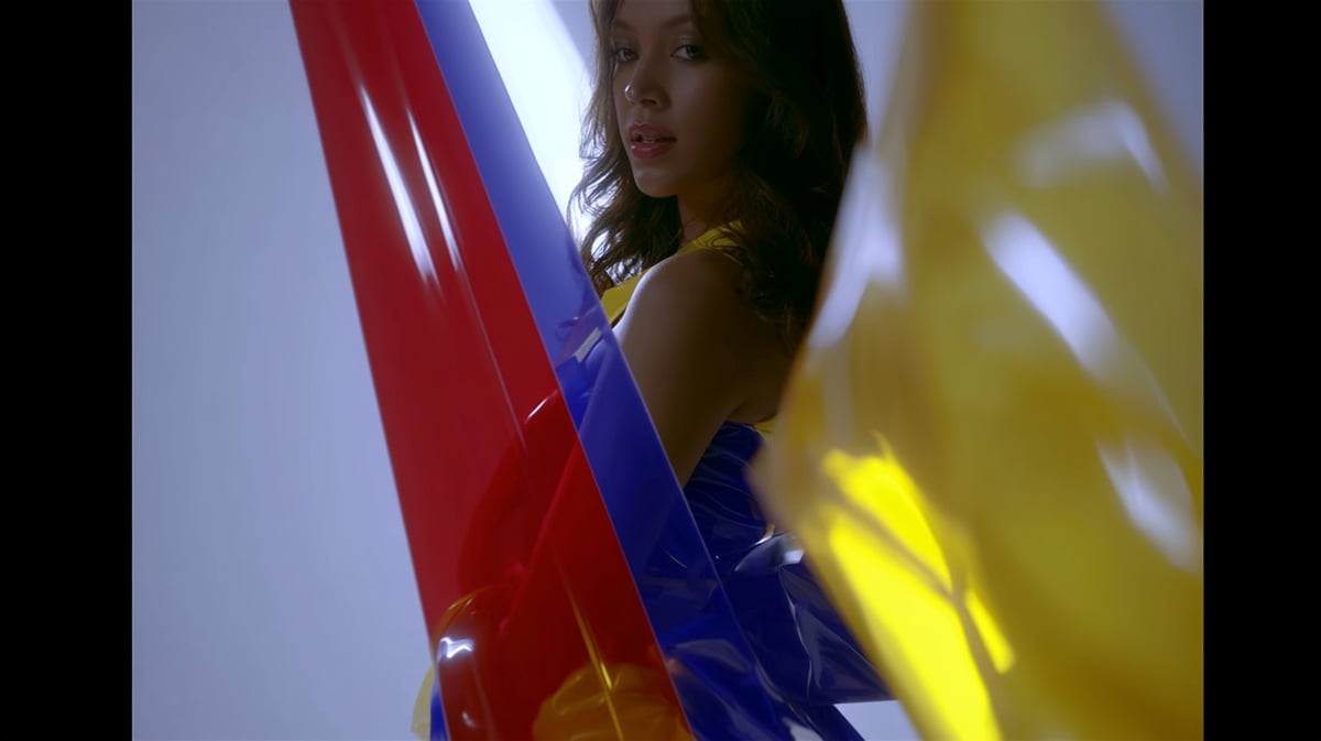 A fast-paced 16:9 cinematic pop-fashion trailer shot. A minimalist white space sliced by sharp, overlapping streaks of pure primary red, royal blue, and bright yellow light. Glossy color-blocked patent leather garments and accessories cutting through the frame with dynamic motion blur. Extreme color saturation, commercial studio lighting, futuristic lookbook aesthetic